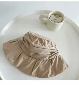 Detail shot of a casual pleated bucket hat in beige, showing soft fabric texture and folds.