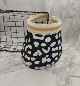 Black and white cow print sun visor detail, woven straw texture, open top design for summer.