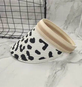 Summer straw sun visor hat close-up, black and white cow print detail and beige band.