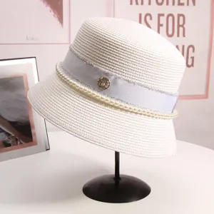 Dettaglio elegante del cappello bianco in paglia con decorazione di perle e logo M.