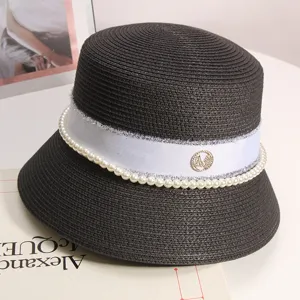 Vista dettagliata del cappello di paglia nero con nastro bianco, perle e logo strass.