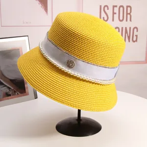 Primo piano del cappello da sole in paglia gialla con nastro bianco, perle e logo M.