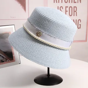 Dettaglio dell'elegante cappello da pescatore in paglia azzurra con perle e logo in metallo.