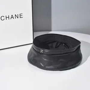 Black PU leather beret detail showing texture, stitching, and metal M logo on white surface.