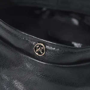 Detail view of a black PU leather beret featuring a stylish metal letter M badge accent.