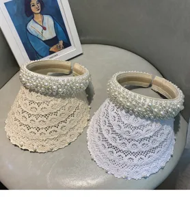 Detail view of pearl-embellished lace empty-top sun visor hats in beige and white.