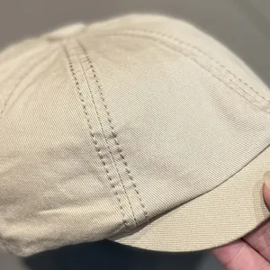 Close-up detail shot of a stylish beige canvas octagonal beret hat, showing neat stitching.
