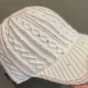 Gros plan détaillé de la casquette de baseball en tricot blanc ornée de strass irisés.