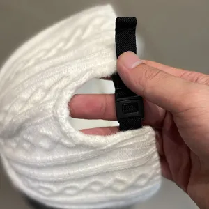 Gros plan detaille montrant la sangle reglable noire et la boucle sur le bonnet en tricot blanc.
