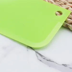 Green plastic dough scraper detail shot, flexible baking tool for pastry and cake crafting.