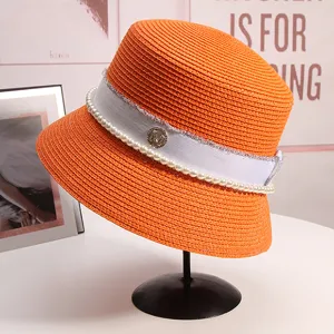 Dettaglio del cappello da sole arancione in paglia con perle eleganti e logo M metallico.
