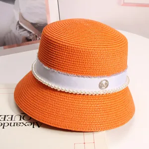 Primo piano del cappello bucket in paglia arancione con perle, nastro bianco e logo strass.