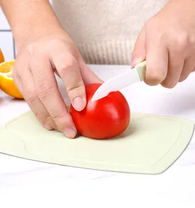 Close-up detail shot of portable ceramic fruit knife and mini cutting board during fruit cutting.