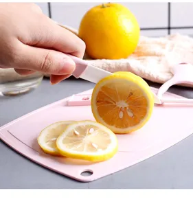 Detail view of ceramic fruit knife cutting lemon on pink cutting board, kitchen tool scene.