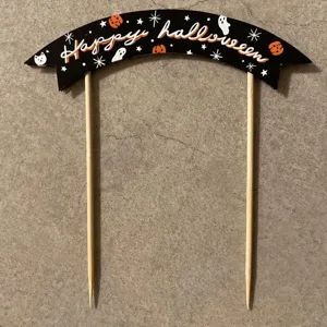 Halloween cake topper with black banner and wooden sticks for spooky party decor.