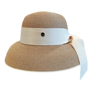 Chapeau de paille élégant pour femme avec ruban nœud en soie blanche et charm métal de soleil.