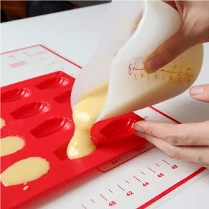 Detail view of transparent silicone measuring cup pouring batter into a red mold during baking.