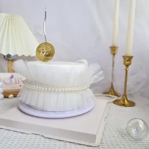 Primer plano detalle del adorno de pastel de acrílico dorado con tul blanco y perlas.