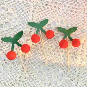 Cherry cake topper detail view, cute fuzzy pom-pom fruit decoration for birthday party treats.