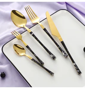 Detailed view of luxury gold stainless steel cutlery set with black marble handle on plate.
