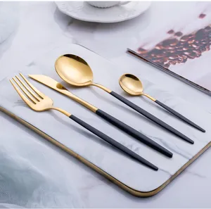 Close-up view of elegant black and gold stainless steel cutlery set on a white marble tray.