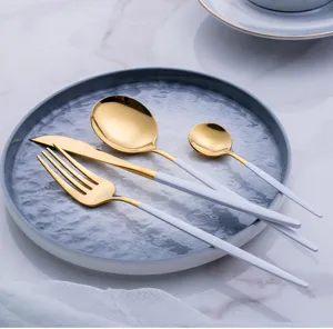 Stainless steel flatware set featuring gold spoons, forks, and knives with elegant white handles.