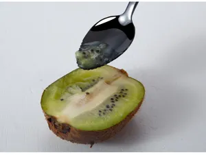 Stainless steel serrated fruit puree spoon detail view showing kiwi fruit scraping process.