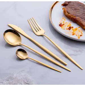 Gold stainless steel flatware set detail showing knife, fork, and spoons on marble table.