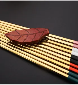 Close-up detail of golden stainless steel chopsticks with colorful ends and wooden leaf rest.