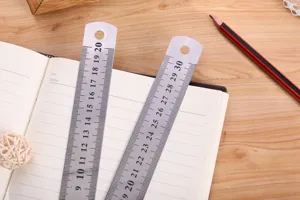 Stainless steel straight ruler detail showing clear metric scale markings on a wooden table.
