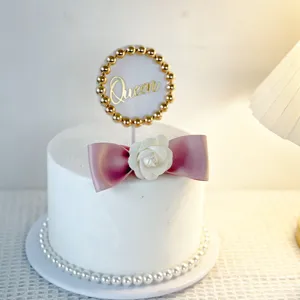 Elegant cake topper detail featuring Queen text, golden beads, and a chic white flower bow.