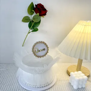 Detailed view of white tulle cake decoration with pearl border and Queen acrylic cake topper.