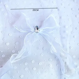 Close-up detail of a white organza ribbon bow with a sparkling rhinestone center for decor.