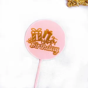 Topper de gâteau rond en acrylique rose avec texte joyeux anniversaire et boîte cadeau dorée.