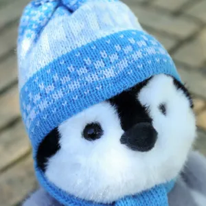 Close-up detail of cute plush penguin wearing a soft blue winter knitted hat and cozy scarf.