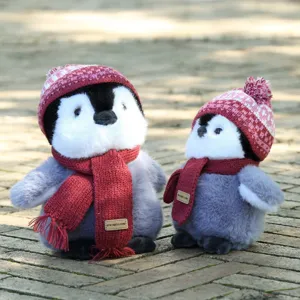 Detail shot of cute penguin plush toy set wearing knitted hats and red scarves on brick background.