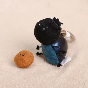 Close-up of cute bug plush toy pendant with small round companion piece on soft surface.