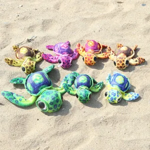 Colorful plush sea turtle toys with hanging ropes, displayed on sand for a detailed view.