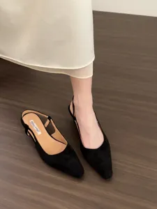 Close-up detail of elegant black pointed toe slingback low heel shoes on clean wooden floor.