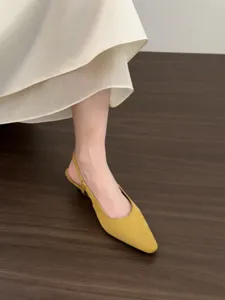Detailed shot of yellow suede pointed-toe slingback kitten heels paired with skirt.