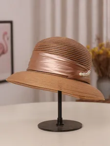 Gedetailleerde close-up van de elegante bruine zonnehoed met glad satijnen lint en parels.
