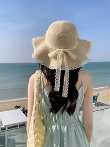 Vue detaillee du chapeau de paille de plage d'ete avec noeud en dentelle et bord ondule.