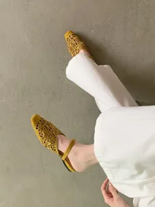 Detail shot of yellow suede cutout square toe flat shoes paired with white pants.