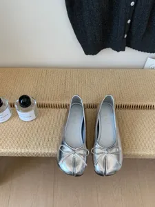 Vista dettagliata di scarpe ballerine argento con punta divisa, fiocco e suola morbida.