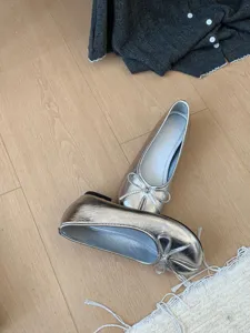 Vista dettagliata di ballerine metalliche argento con fiocco, suola morbida e design slip-on.