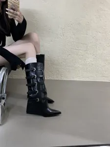 Detail view of black wedge knee-high boots with buckle straps and stylish pointed toe design.