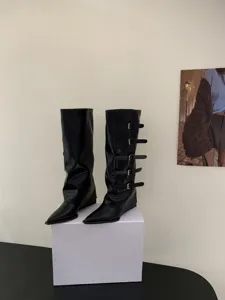 Detail shot of black pointed toe knee high boots with multiple buckle straps and wedge heel.