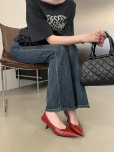 Detailed shot of elegant red pointed kitten heel shoes paired with denim jeans and handbag.