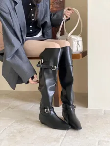 Detail shot of black slouchy knee-high boots featuring square toe, flat heel and metal buckles.