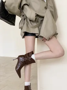 Vista detallada de las botas de tacón con punta fina, diseño plisado y hebilla elegante.